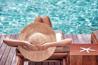 women sitting by a pool relaxing with a straw hat 