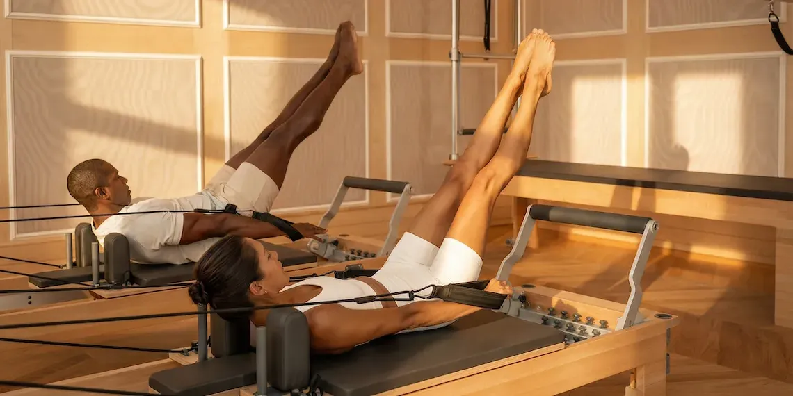 man and woman doing Pilates on wooden reformer machines