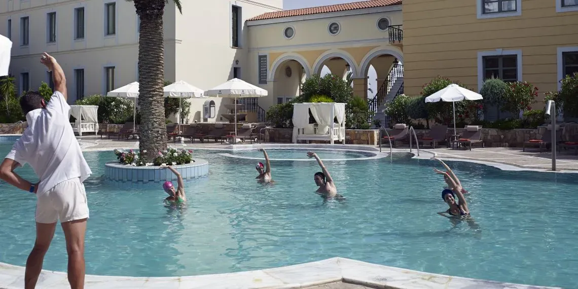 instructor outside pool showing pose to people in outdoor pool