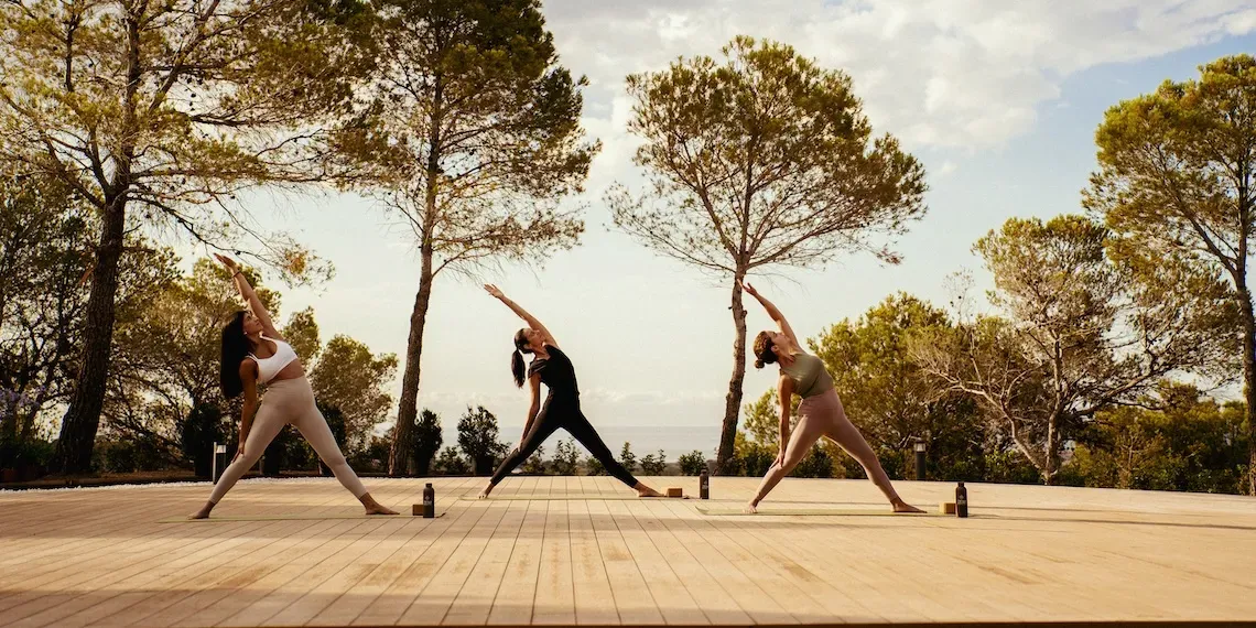 three woman in yoga pose on outdoor deck in front of trees