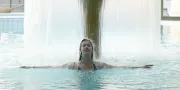 lady in a pool underneath a water stream